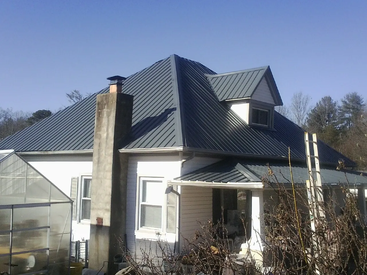 Dark blue standing seam metal roof on a white farmhouse with dormer — Slate & Tile Roof Repair by Roofing Brothers in Novelty