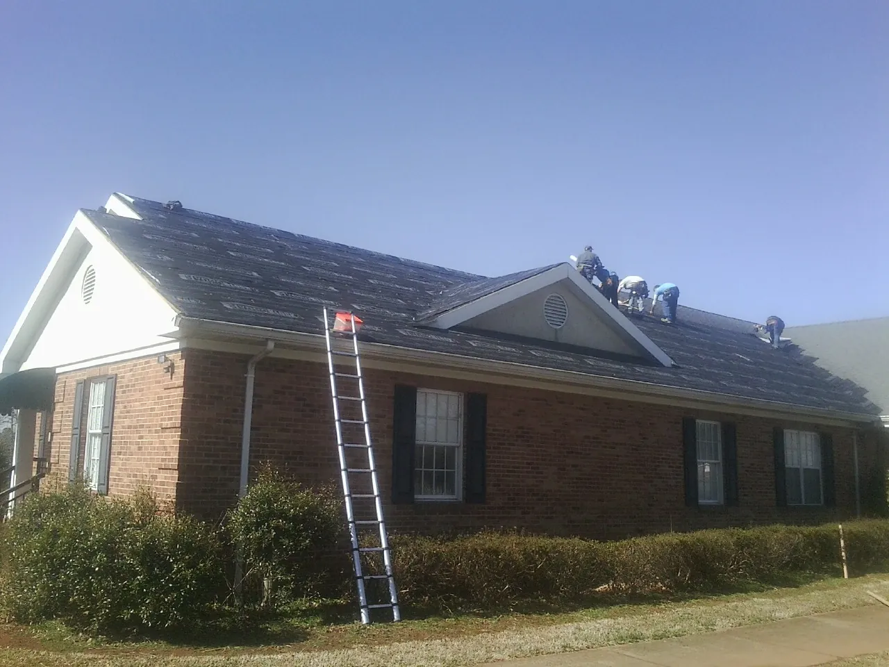 Crew tearing shingles off a brick ranch roof with a ladder set — Emergency Roof Repair work by our crew in Novelty
