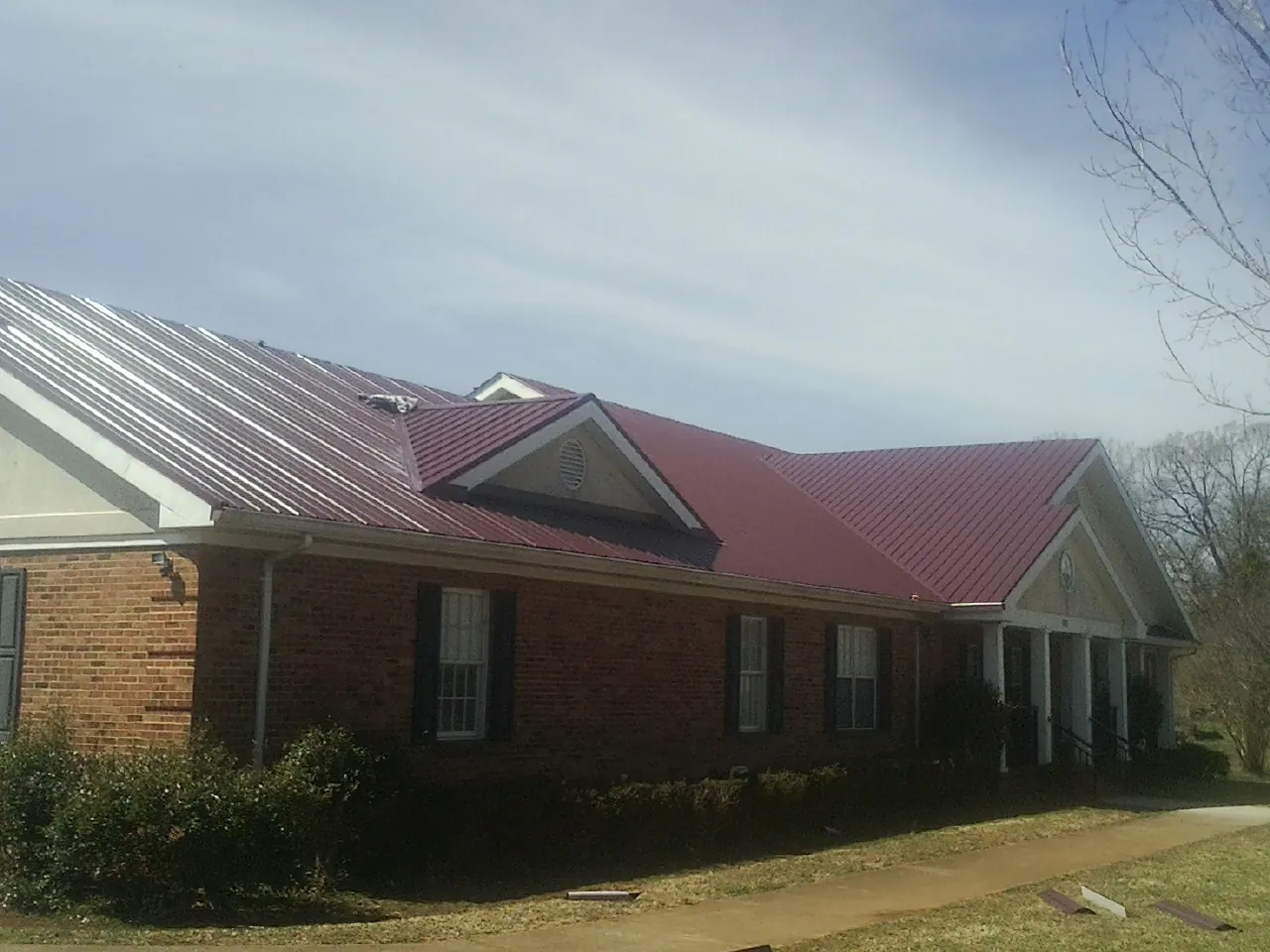 Red metal roof with gabled entries on a long brick building, from a Hail Damage Roof Repair job in Novelty