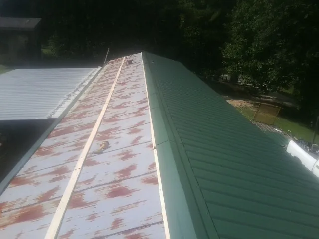 Old rusted panels beside newly installed green metal roofing — Wind Damage Roof Repair by Roofing Brothers in Novelty