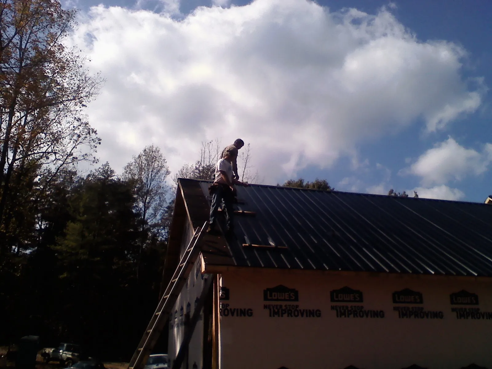 Roofer fastening dark metal panels high against a cloudy sky, from a Roof Inspection job in Novelty