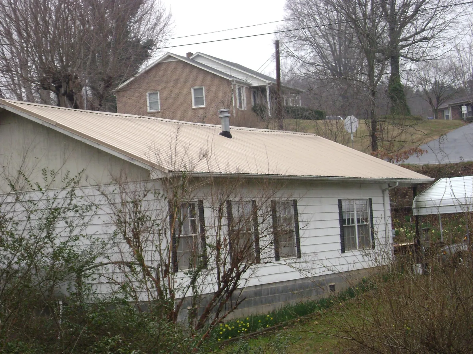 Tan metal roof on a white sided house set into a hillside — Commercial Roofing by Roofing Brothers in Novelty