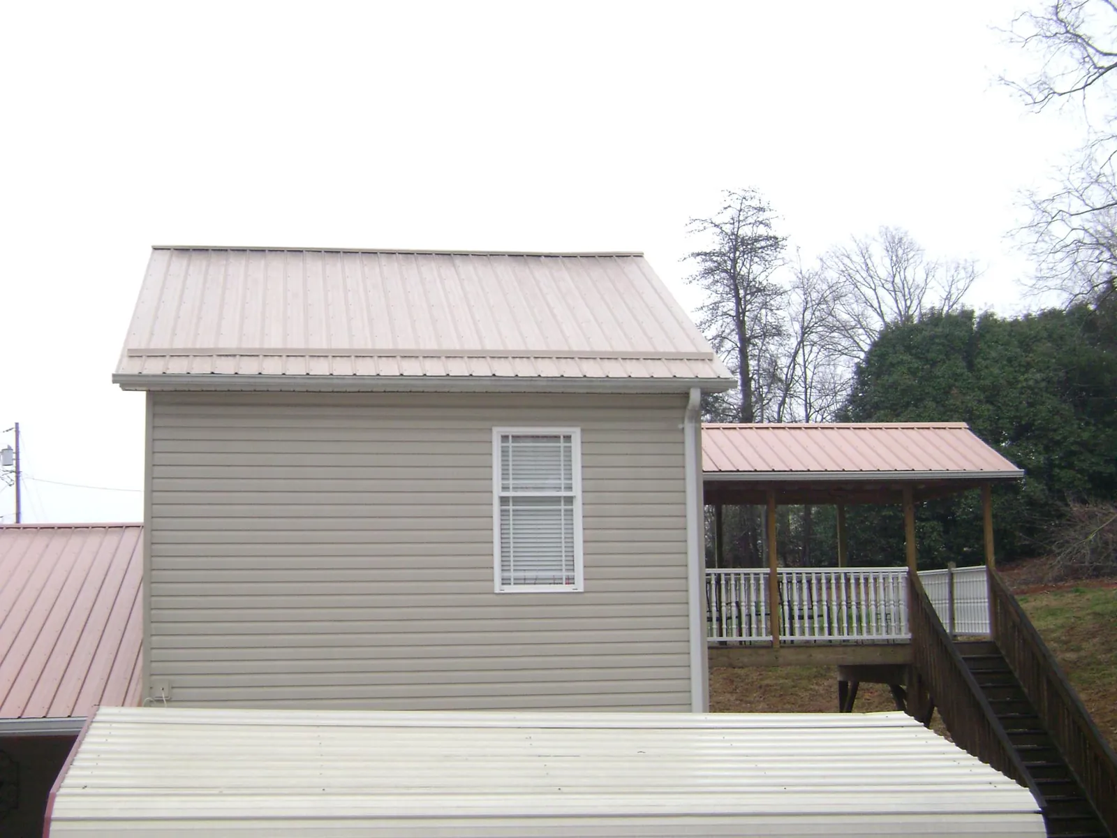 Tan metal roofs on a two story addition and attached porch, from a Roof Replacement job in Novelty